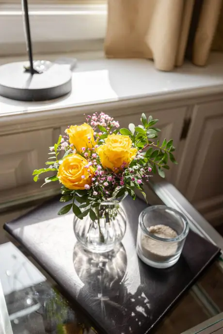 Ein Strauß gelber Rosen auf einem Tisch mit einem Glas mit Kerze in der Nähe im 12.18. Hotel Stadt Hamburg.