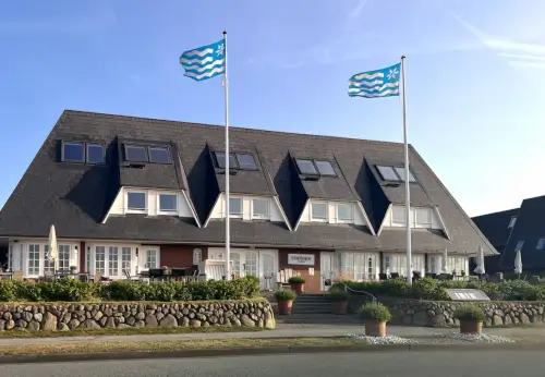 12.18 Hotel Stadt Hamburg in Kampen, Sylt, mit zwei Flaggen und einem einzigartigen Dach mit Blick auf üppige Pflanzen.