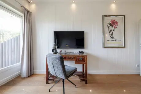 Stilvolles Hotelzimmer mit Schreibtisch, Fernseher und einem grauen Stuhl.