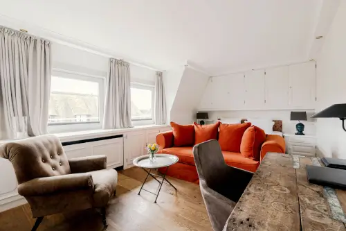 Gemütliches Hotelwohnzimmer mit orangefarbenem Sofa und Arbeitsbereich im Hotel Stadt Hamburg, Sylt.