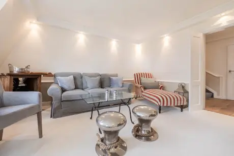 Stilvolles Hotellounge mit grauem Sofa, gestreiftem Stuhl, Glastisch und metallischen Hockern.
