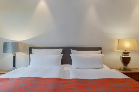 Gemütliches Hotelzimmer mit einem Doppelbett, stilvollen Lampen und einem orangen Bettbezug im Hotel Stadt Hamburg.