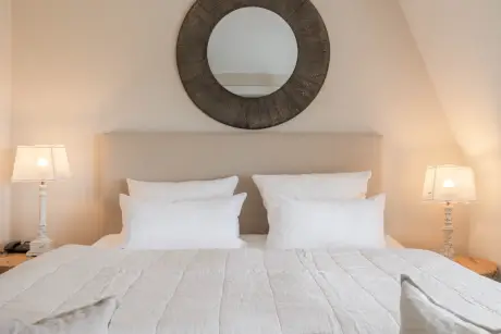 Stilvolles Hotelzimmer mit gemütlichem Bett, eleganten Lampen und einem runden Spiegel im Hotel Stadt Hamburg.