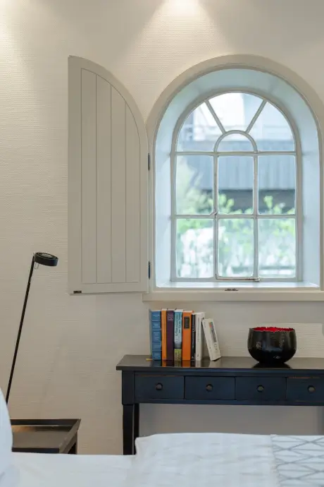 Stilvolles Hotelzimmer mit dekorativem Fenster, Schreibtisch und Bücherregal.