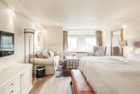 Elegantes Hotelzimmer mit Sofa, Fernseher und großen Fenstern für viel Licht.