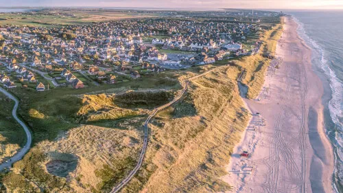 Luftaufnahme des Strands und der Dünen bei Kampen, Sylt, umgeben von malerischen Häusern.