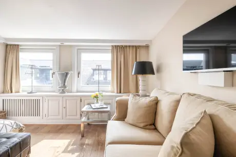 Gemütliches Wohnzimmer mit beigem Sofa, eleganter Lampe und modernem Fernseher im Hotel Stadt Hamburg.