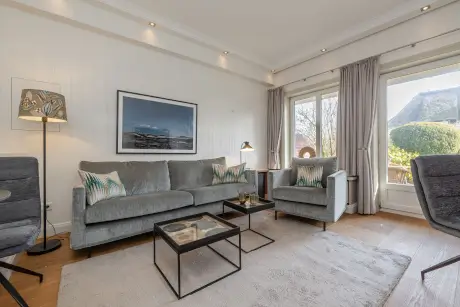 Ein gemütliches Wohnzimmer mit einem grauen Sofa und moderner Lampe für einen komfortablen Aufenthalt im 12.18. Hotel Stadt Hamburg.